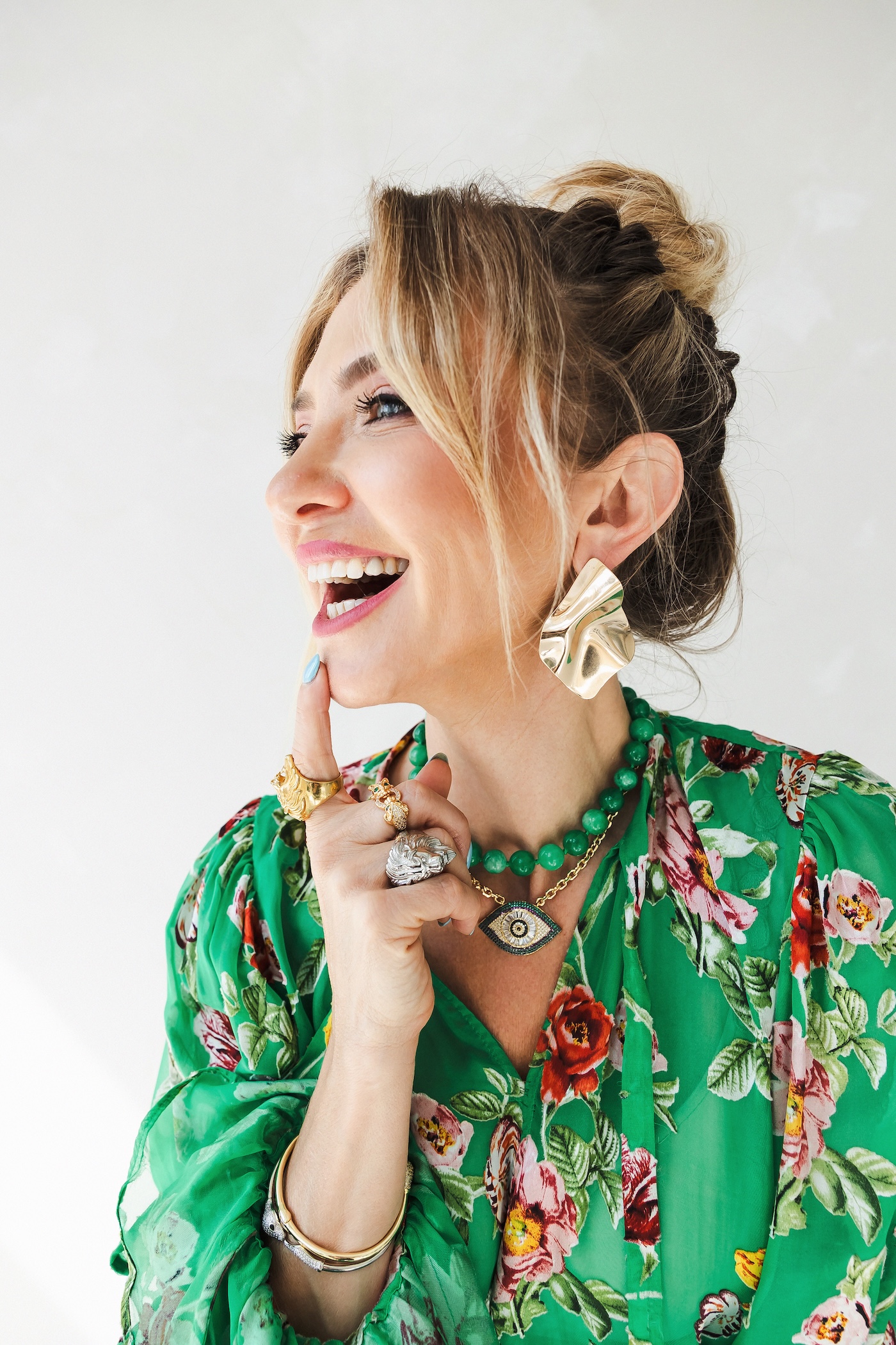 Smiling woman in a green floral dress adorned with bold jewelry.